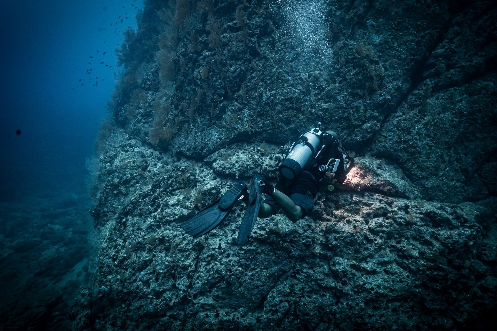 Jalvan diving against a massive rocky wall in Bahía Solano, using a light to search a crevice for macro marine life.