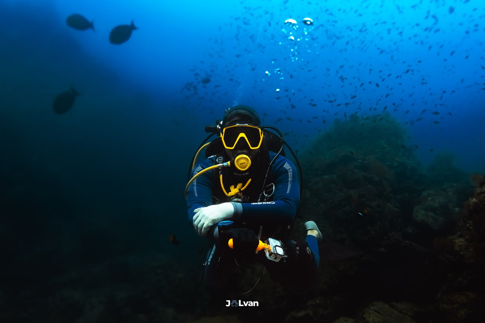 A scuba diver with a yellow mask and fins posing with arms crossed while hovering over a rocky reef in Bahía Solano.