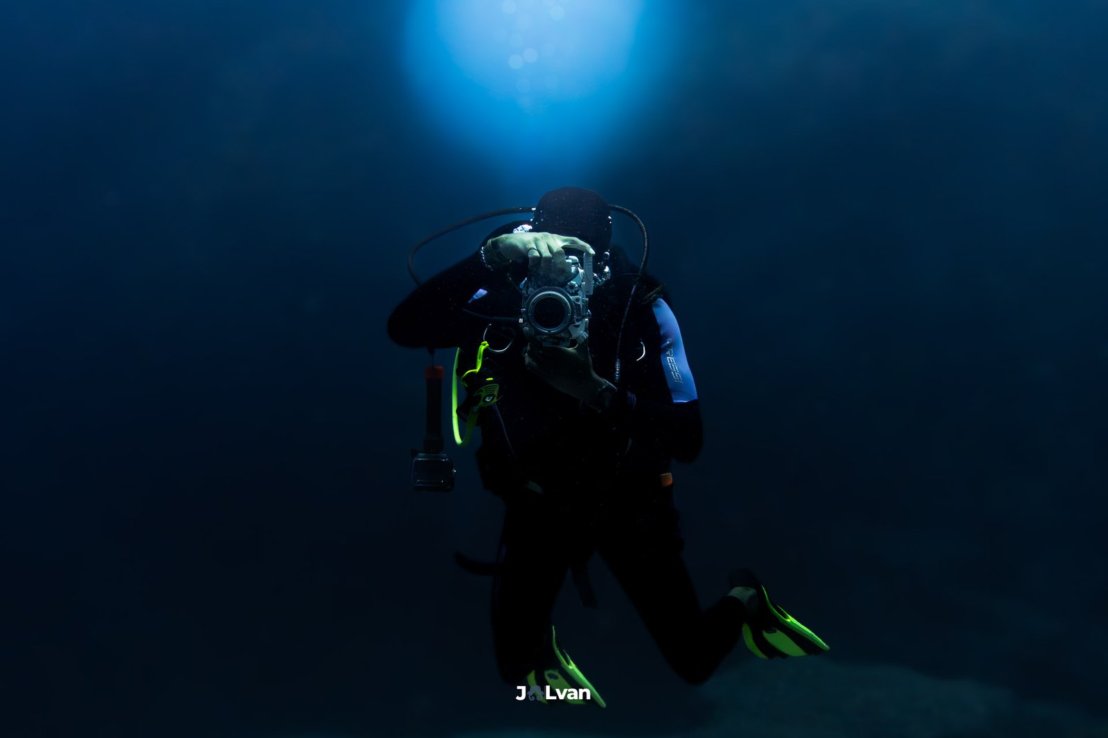 Dramatic silhouette of an underwater photographer taking a picture with a large camera rig against the surface sunlight.